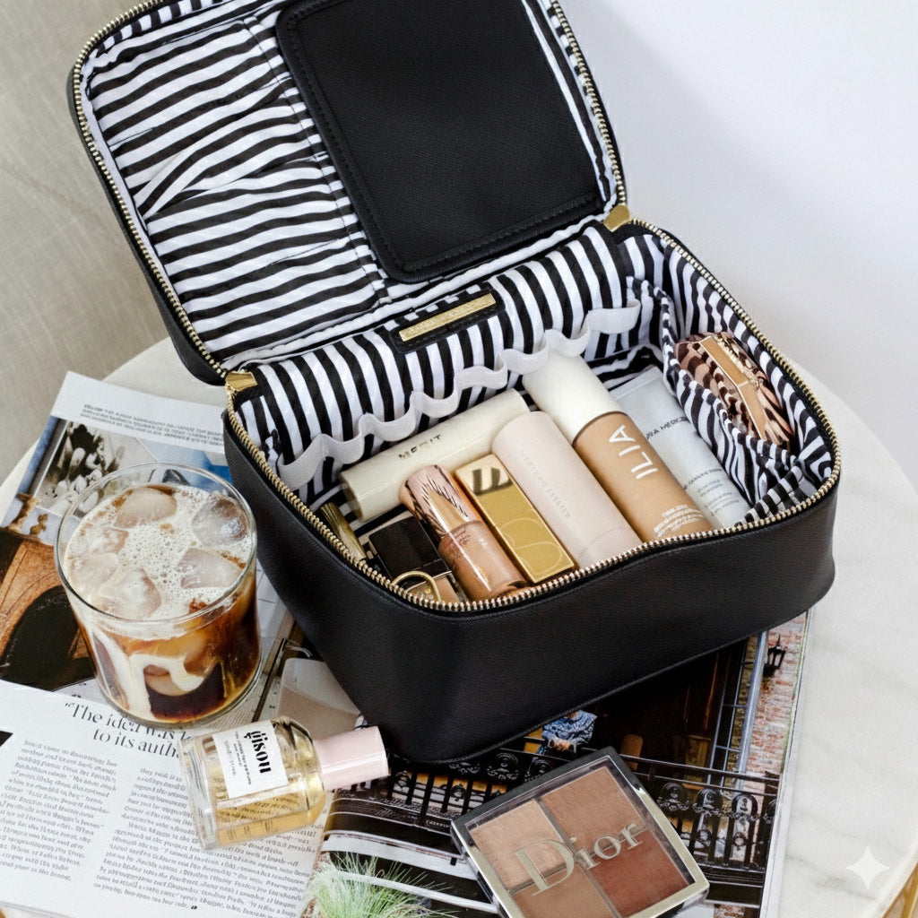 Black and white striped makeup case with cosmetic products on a table with a glass of iced coffee.